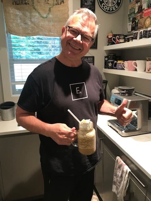 Rick in the café kitchen holding up a tall iced coffee
